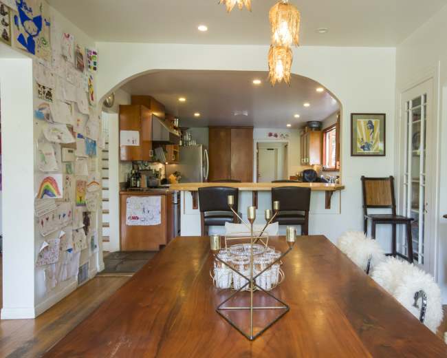 A dining area with a wooden table, a kitchen in the background, and walls decorated with children's artwork.