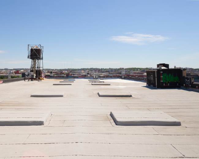 A flat rooftop features several rectangular skylights and a communication tower in the background against a clear blue sky.
