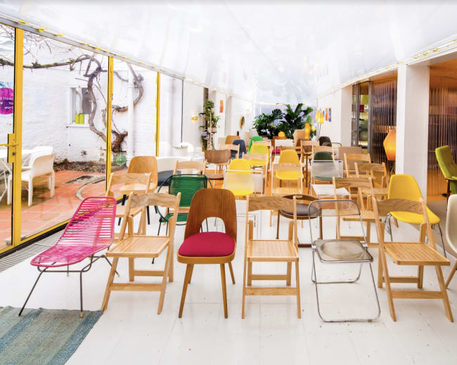 A spacious interior featuring an array of colorful chairs arranged in a line, with large windows allowing natural light to fill the room.