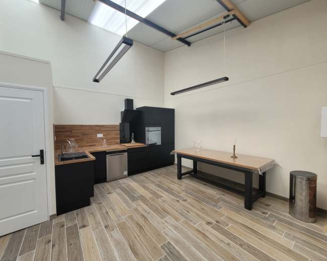 The image shows a modern kitchen with black cabinetry, wooden accents, and a central table on a tiled floor.
