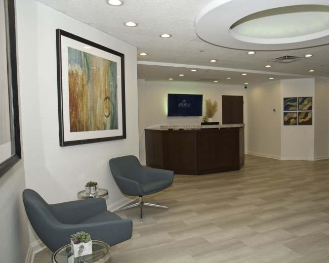 A modern reception area with two gray chairs, a front desk, and artwork hanging on the walls.