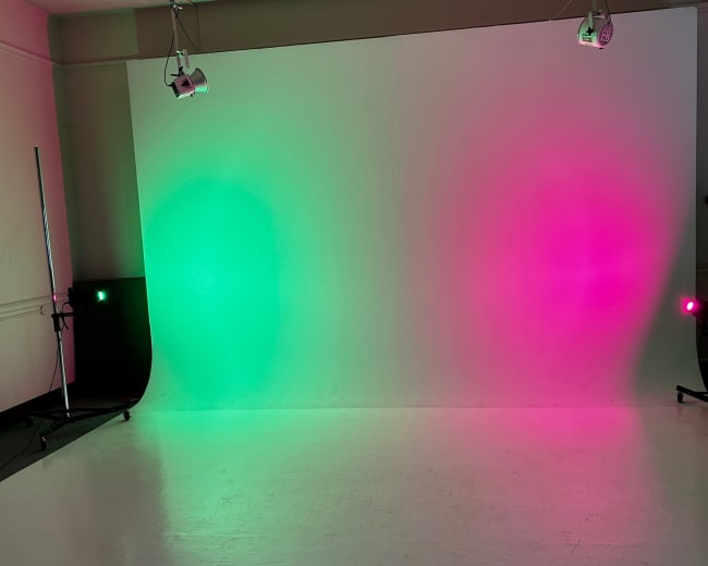 The image shows a photo studio with a blank backdrop illuminated by green and pink lights.