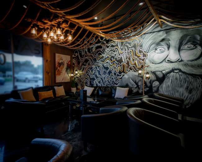 The image shows a modern lounge with leather seating, a prominent decorative mural on the wall, and stylish lighting fixtures overhead.