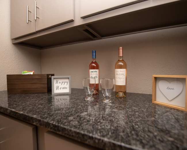 A wooden countertop displays two bottles of wine, glasses, a box, and framed decorative items.