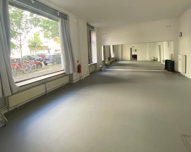 The image shows an empty room with large windows, a mirror on one wall, and smooth gray flooring.