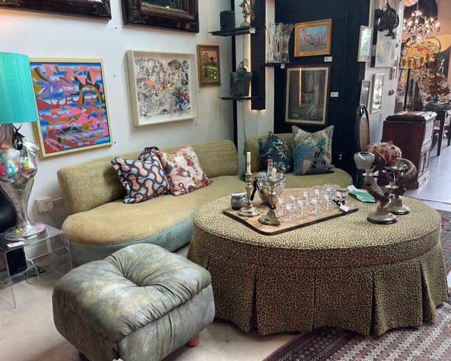The image shows a living area with a curved sofa, a circular coffee table with a leopard print skirt, decorative pillows, and various artworks on the walls.