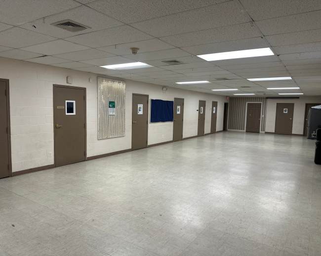 The image shows a long indoor hallway with several closed doors on either side and a blue curtain hanging on the left wall.