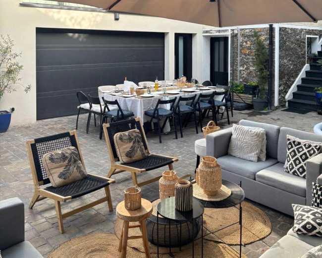 A patio area features a dining table set for a meal, surrounded by seating and sheltered under a large umbrella.