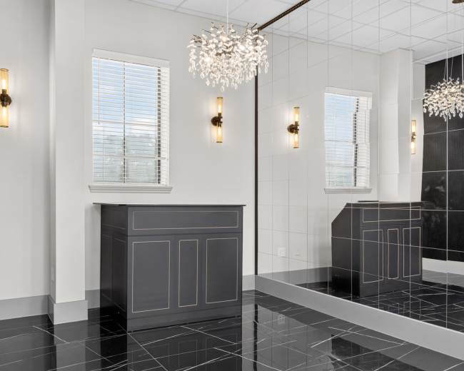 The interior features a sleek black and white design with a mirrored wall, a chandelier, and a vanity unit underneath the windows.