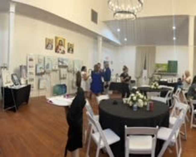 A large group of people gathers in a well-lit event space filled with tables and art displays.