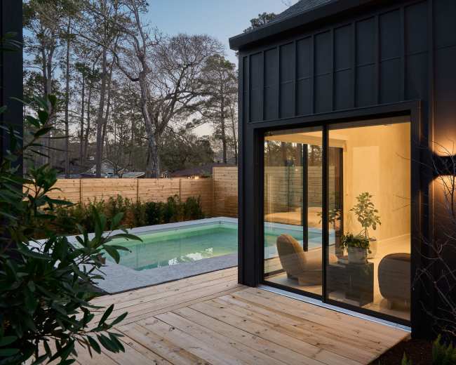 A modern home features a glass door opening to a backyard with a swimming pool surrounded by wooden fencing and trees.
