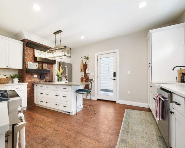 A modern kitchen features white cabinets, a stone accent wall, a central island with seating, and a door leading to an outdoor area.