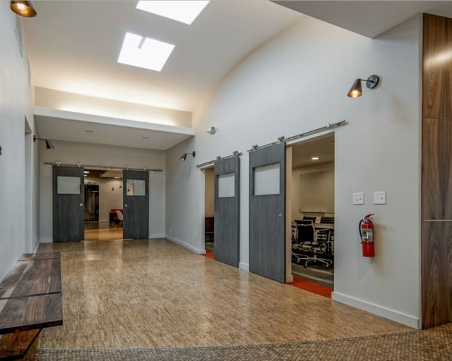 A modern hallway with sliding barn doors leading to meeting rooms and a wooden bench along one side.