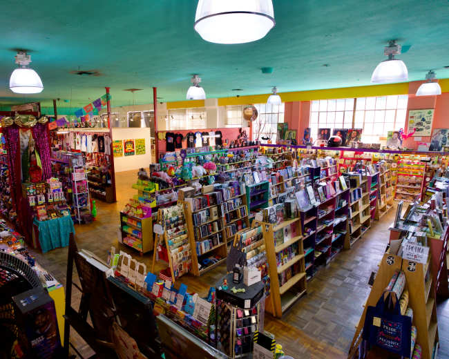 The image shows an expansive and colorful gift shop filled with shelves of books, toys, and various novelty items under bright lighting.