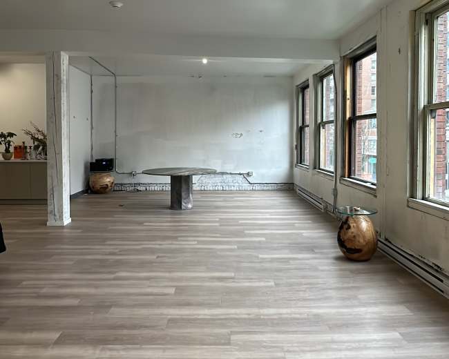 A spacious, empty room with wooden floors, large windows, and a simple table in the center.