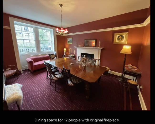 A dining room featuring a wooden table set for twelve, an original fireplace, and a mix of lighting fixtures.