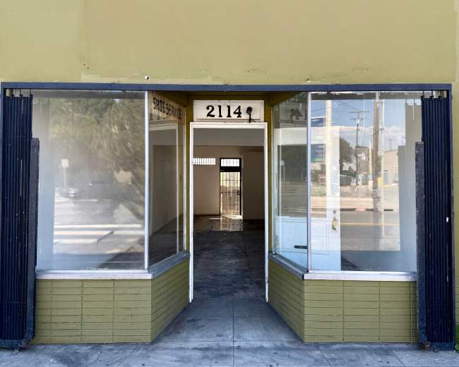 The image shows a vacant storefront with large windows on either side and a clear view into the empty interior.