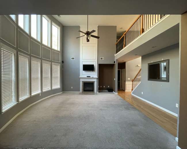 A spacious living room with tall windows, a central fireplace, and an open layout that connects to an upper level.