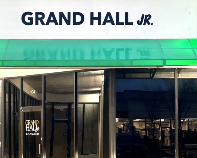 The exterior of a storefront labeled "GRAND HALL JR." with large glass windows and a green awning.