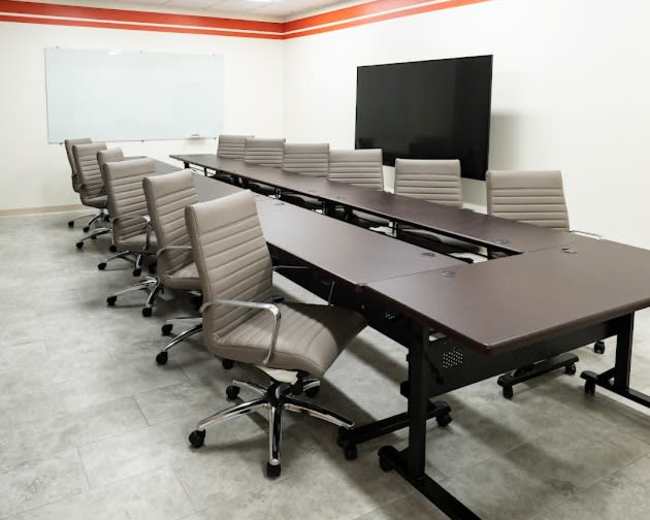 A modern conference room features a long table with multiple ergonomic chairs, a large screen, and whiteboard on the walls.