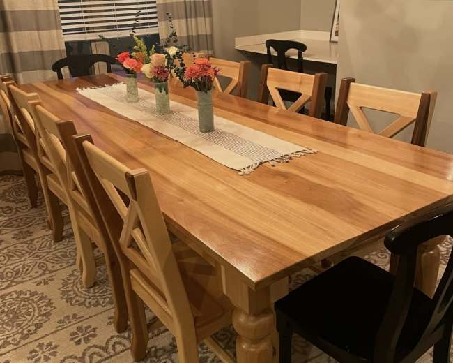 A long wooden dining table is set with a runner and vases of flowers, surrounded by chairs of varying designs.