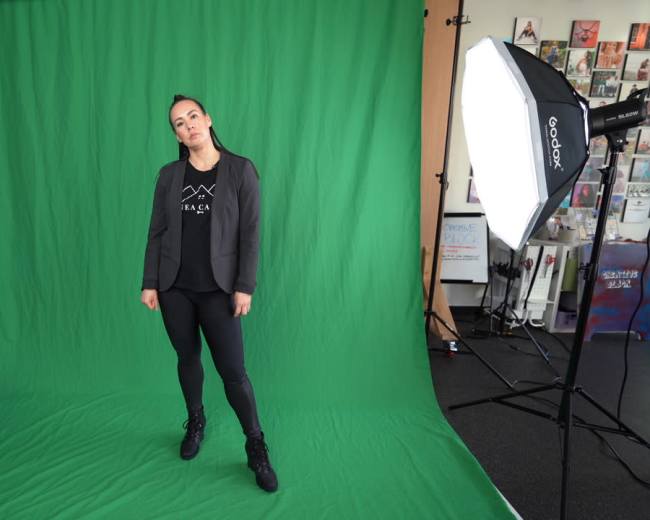 A person stands in front of a green backdrop with studio lights positioned on either side.