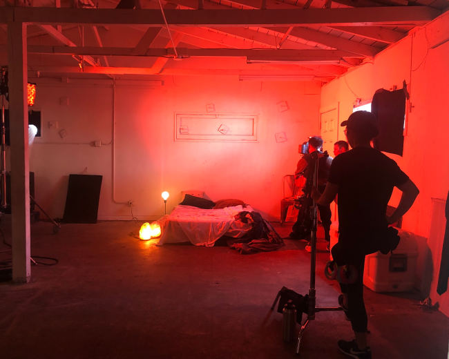 A dimly lit room featuring a bed, props, and various lighting equipment set up for a shoot.