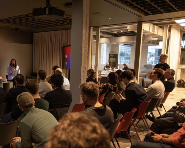 A panel discussion is taking place in a modern conference room, with attendees seated and focused on the speakers at the front.