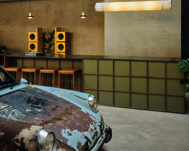 The image shows a stylish interior with a bar featuring a vintage car displayed in front of it, paired with modern lighting and furniture.