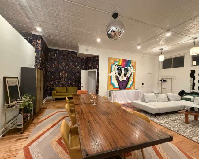 The image shows a modern interior space with a dining table, a seating area, and vibrant artwork on the walls.