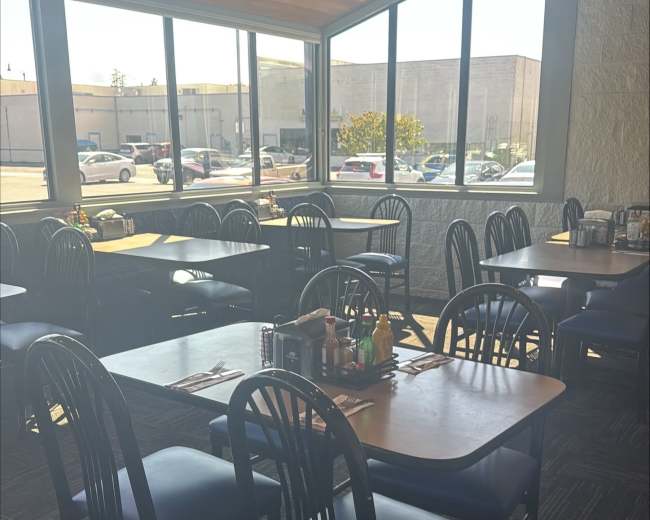 The image shows an empty restaurant interior with several tables and chairs arranged near large windows.