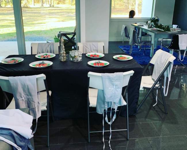 A dining table is set with plates of food, surrounded by folding chairs and adorned with decorative items in a modern room with large windows.