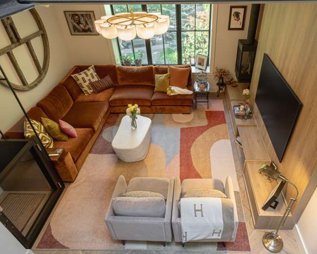 The image shows a cozy living room featuring a large brown sectional sofa, a light-colored coffee table, and two armchairs arranged on a decorative area rug.