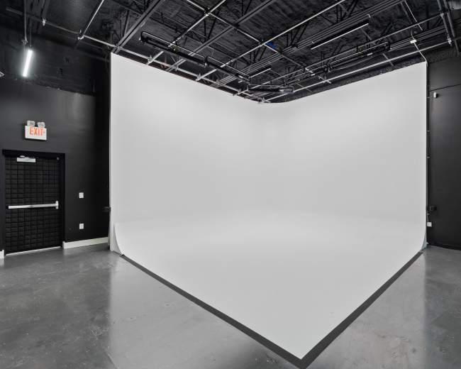 The image shows a spacious photo studio with a white cyclorama wall and a black ceiling.