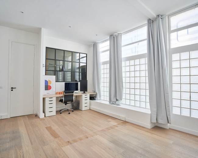 The image shows a modern office space with a desk and computer, large glass block windows, and light-colored wooden flooring.