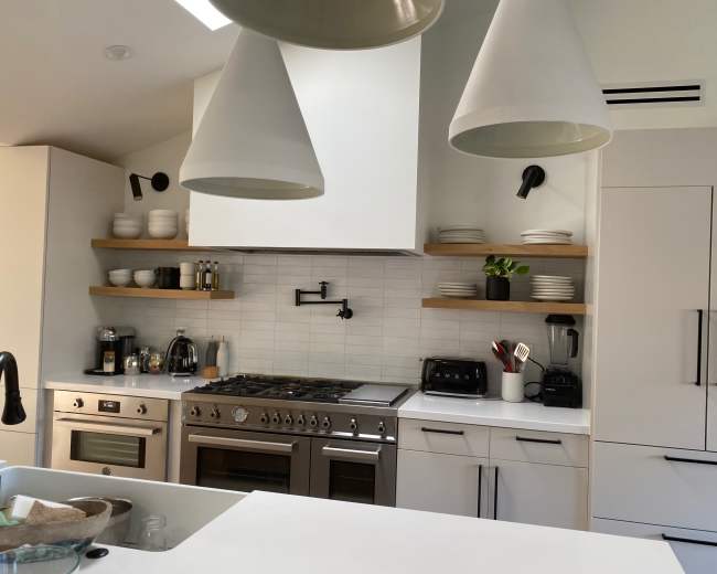 The image shows a modern kitchen with stainless steel appliances, open shelving with dishware, and a large gas stove.