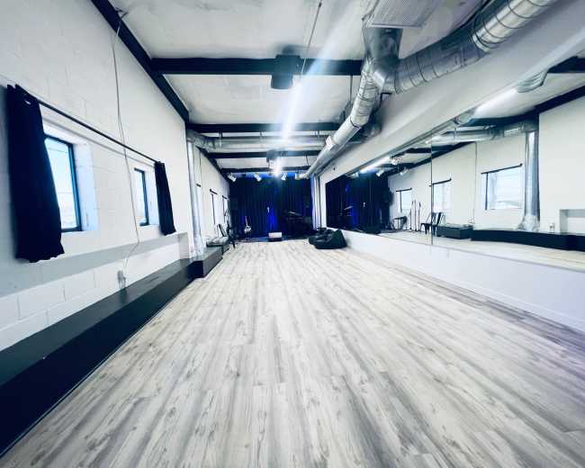 A spacious dance studio with wooden flooring, large mirrors, and a dark curtain backdrop.