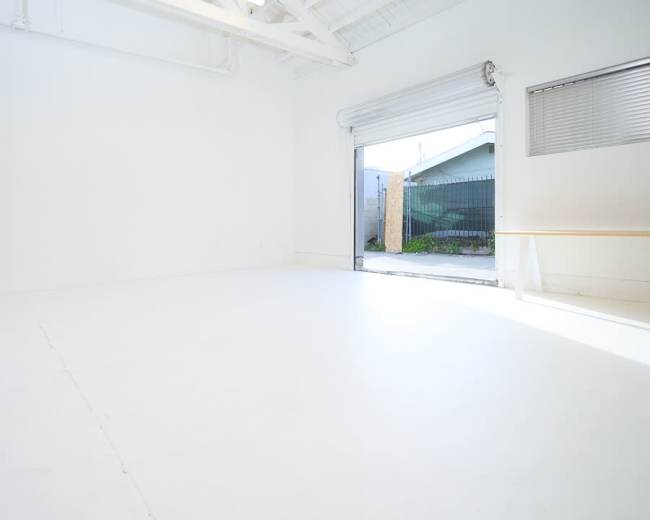 A spacious, empty room with white walls and a large open door leading to an exterior area.