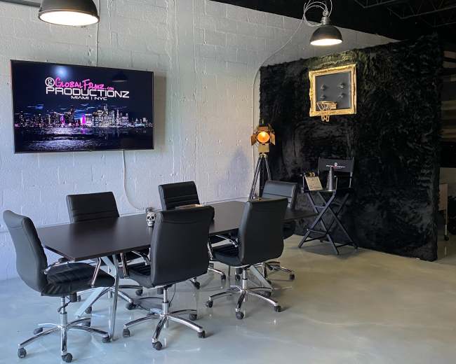 A conference room with a black table and six chairs is shown, featuring a large TV displaying "Global Plane Productionz" and a wall with a basketball hoop and spotlight.