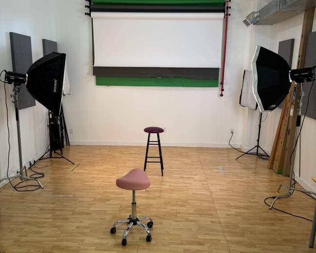 The image shows a studio space with two chairs and several lighting setups surrounded by soundproof panels.