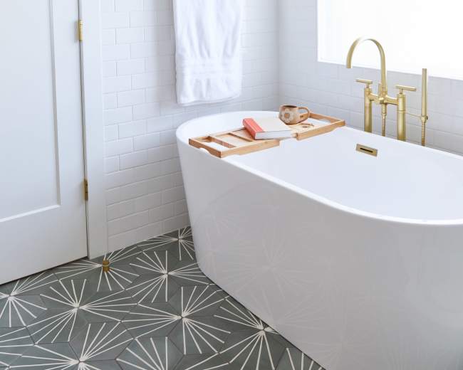 The image shows a modern bathroom featuring a freestanding white bathtub, a hanging plant, a towel rack with a white towel, and stylish tiles with a geometric pattern.