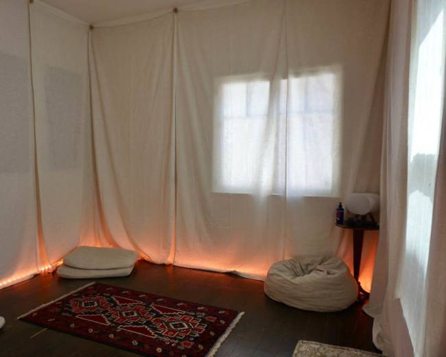 The room features soft floor seating, a decorative rug, and fabric draped along the walls, with ambient lighting along the base.