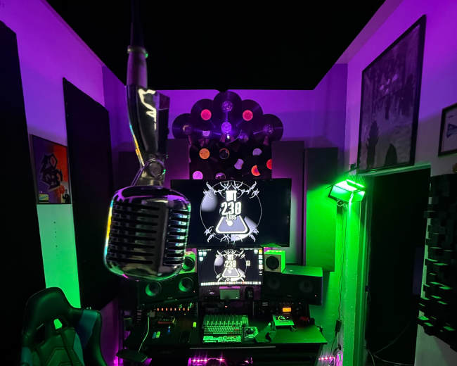 The image depicts a colorful music studio featuring a vintage microphone, a computer screen displaying a visualizer, and various audio equipment illuminated by purple and green lights.