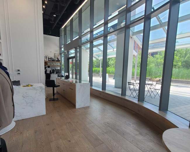 The image shows a modern retail space with large glass windows, minimalistic white furnishings, and wooden flooring.