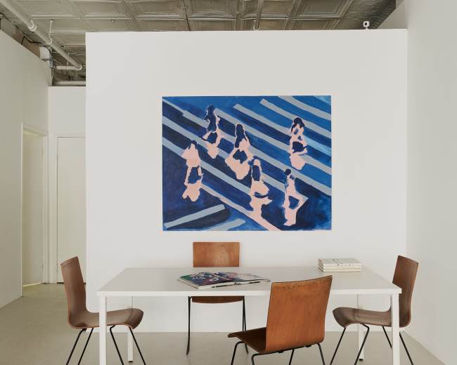 A minimalist interior features a white table surrounded by four chairs, with a large blue and pink abstract painting on the wall.