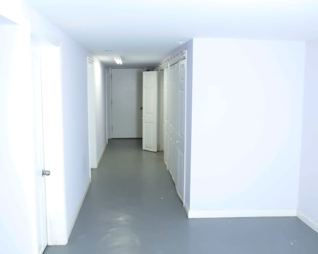 The image shows a corridor with light blue walls, a gray floor, and multiple closed doors along one side.