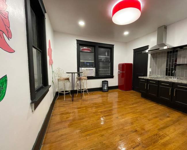 A modern kitchen features dark cabinetry, a red refrigerator, and a small dining area with two chairs against a wall.