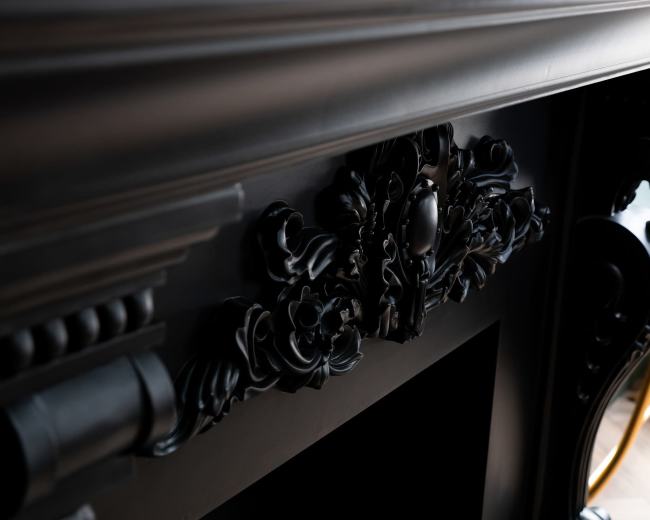 The image shows a detailed black mantelpiece adorned with ornate floral carvings.