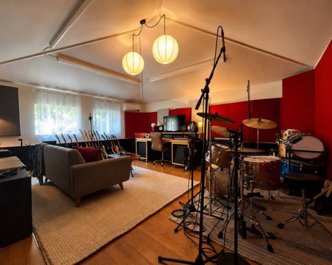 The image shows a well-equipped music studio with various instruments, including a drum set, and a comfortable seating area.