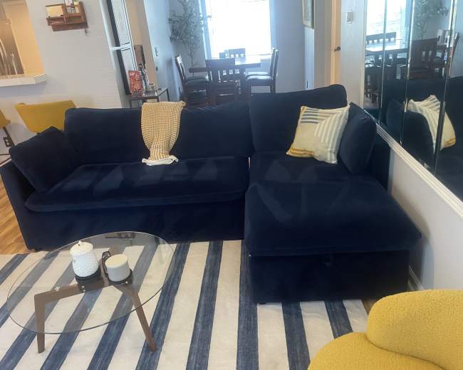 The living room features a dark blue sectional sofa, a glass coffee table, and a yellow accent chair, arranged on a striped rug.